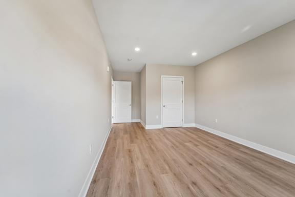 A long, empty hallway with wood flooring and white walls.