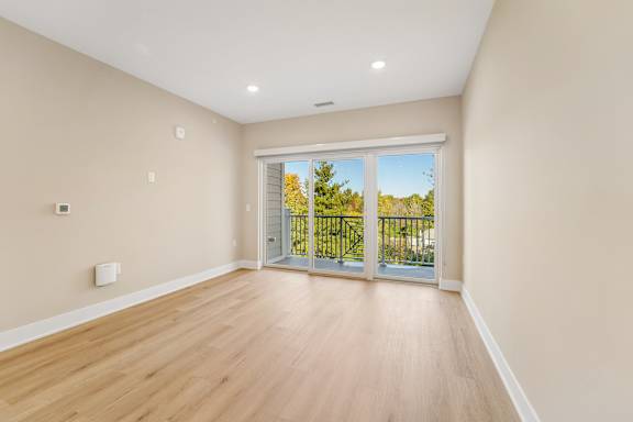 A room with wooden floors and a sliding glass door leading to a balcony.