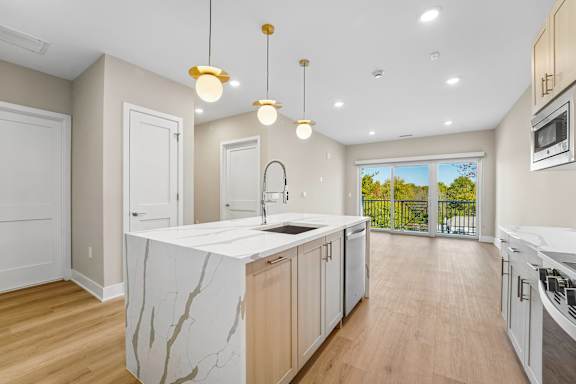 A modern kitchen with a marble island and pendant lights.
