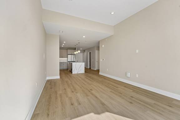 A spacious room with wooden flooring and a kitchen area in the background.