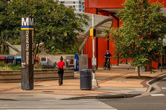 A man in a red shirt is walking past a Crystal City metro station sign.
