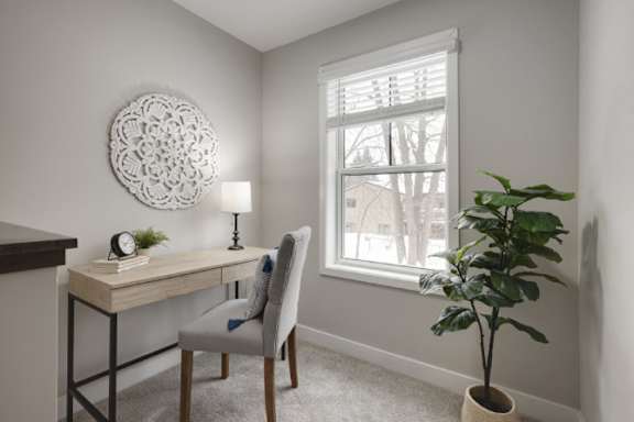 A room with a desk, chair, and a plant.