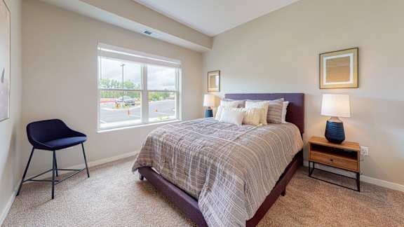 A bedroom with a bed, chair, and window.