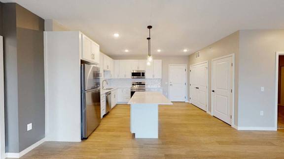 A modern kitchen with a central island and a refrigerator on the left.