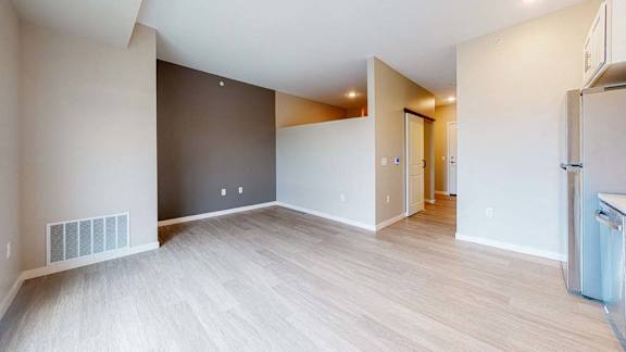 A room with a wooden floor and a white wall with a doorway leading to another room.