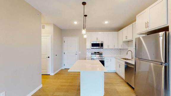 A modern kitchen with a stainless steel refrigerator and wooden flooring.