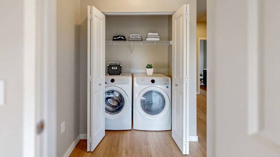A laundry room with two washing machines and a shelf with towels and a plant.