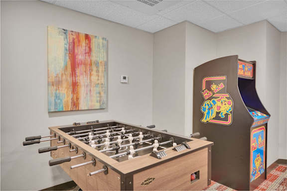 A foosball table sits next to a vintage arcade machine.