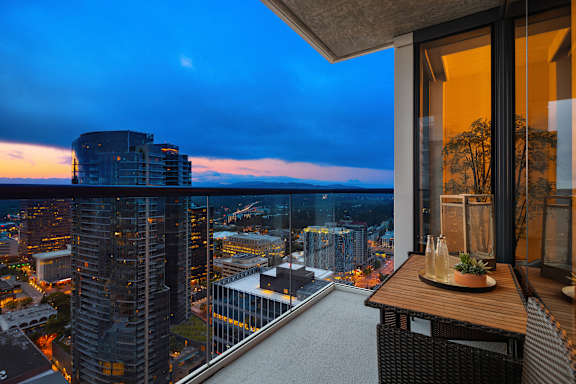 A balcony with a table and chairs overlooking a cityscape at dusk.