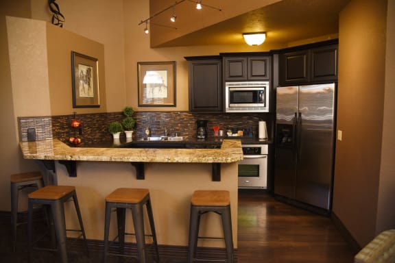A kitchen with a granite countertop and bar stools at Graymayre Crossing Apartments, Spokane, WA