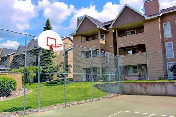 A basketball hoop is mounted on a chain link fence in front of apartment buildings at Graymayre Crossing Apartments, Spokane, WA