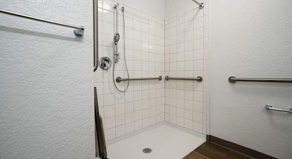 A white tiled shower with a drain in the middle.