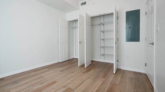 A room with white walls and wooden flooring, featuring a built-in shelving unit and a doorway leading to another room.
