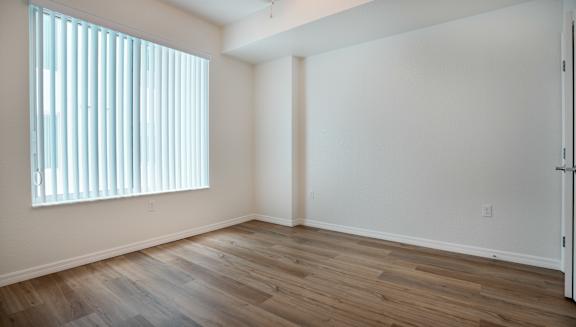 A room with wooden flooring and a window with blinds.