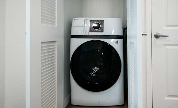 A white washing machine is tucked into a small space between a door and a wall.