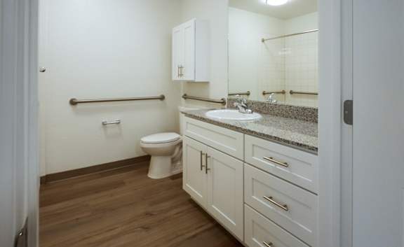 A white bathroom with a toilet, sink, and cabinets.