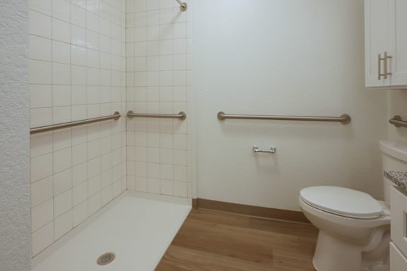 A white toilet sits in a bathroom with white tiled walls and a white bathtub.
