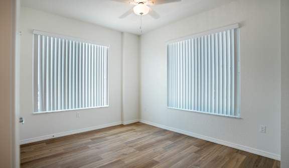 A room with wooden floors and two windows covered with blinds.
