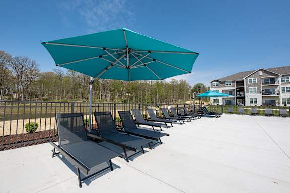 a row of lounge chairs under an umbrella on a white patio at The Bend, Lancaster, Ohio