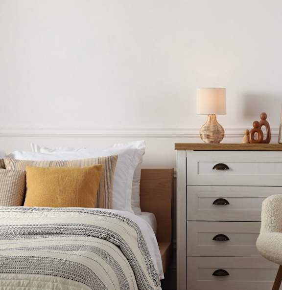 A bed with a yellow pillow and a grey blanket is in front of a white wall.