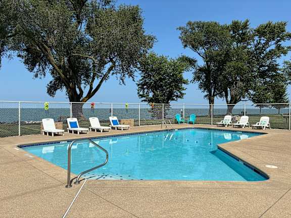 A pool surrounded by trees and chairs.