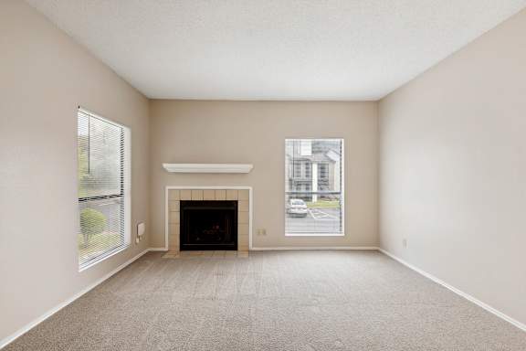 A large, empty room with a fireplace and a window overlooking a parking lot.