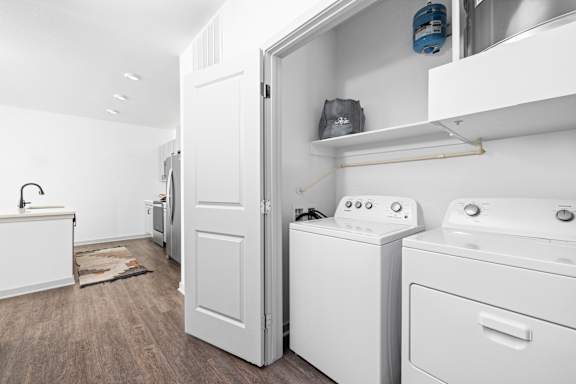 a white laundry room with washer and dryer and a door to a kitchen