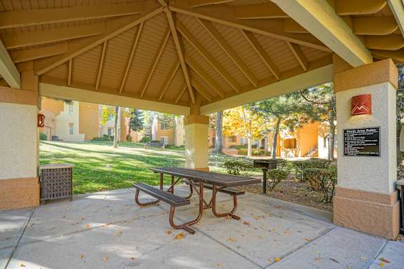 A picnic table is under a shelter on a sunny day.
