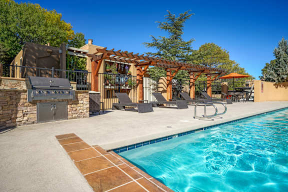 A pool with a grill and a pergola.