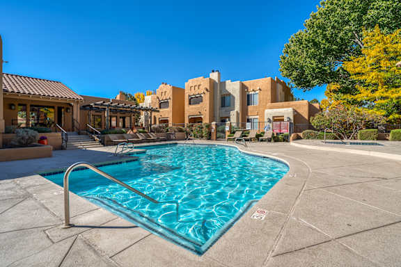 A swimming pool surrounded by a concrete patio and buildings in the background.