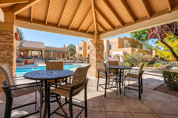 A patio with a table and chairs under a wooden roof.