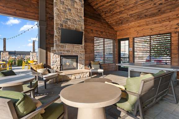 A cozy outdoor seating area with a stone fireplace and a flat screen TV mounted on the wall.
