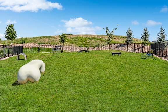 A white sculpture of a done is sitting on the grass in a dog park.