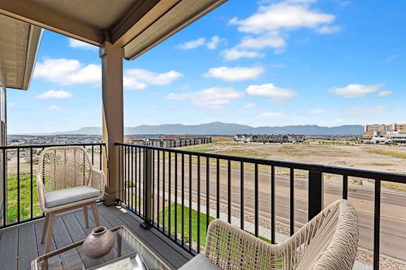 A balcony with two chairs and a table overlooking a highway and mountains.