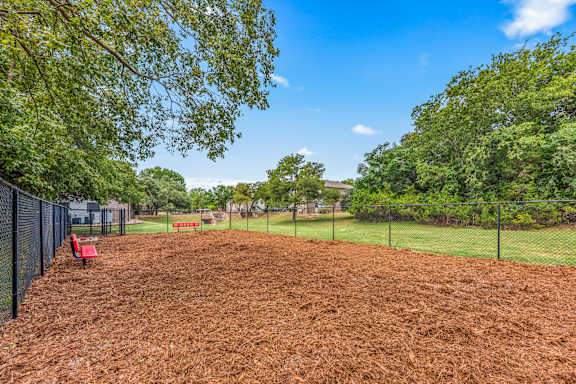 A dog park with a red bench and a black fence.