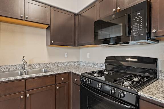 A black microwave is mounted above a black stove in a kitchen.