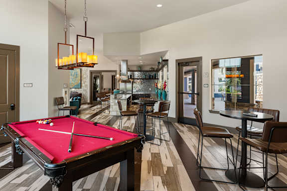 A pool table is in the middle of a room with a bar and chairs.