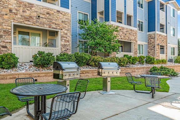 A patio with a table, chairs, and two grills in front of a building.