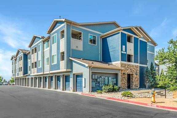 A blue and white apartment building with a parking lot in front.