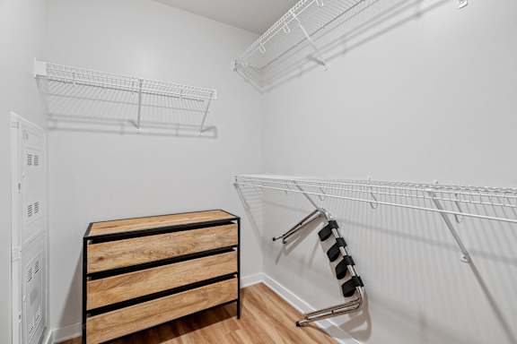 A white closet with a wooden chest of drawers and a metal rack.