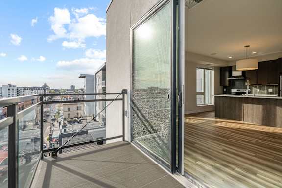 A modern balcony with a glass door leading to a kitchen.