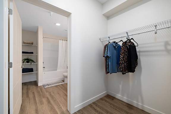 A white closet with clothes hanging on a rail.