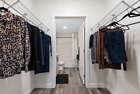 A hallway with clothes hanging on racks and a toilet in the background.