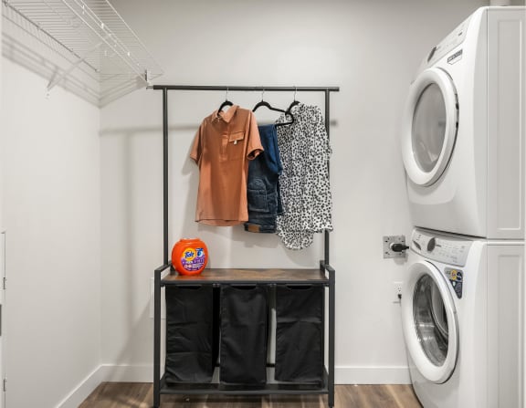 a laundry room with a washer and dryer and a shelf with clothes hanging