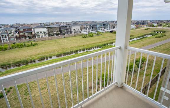 A white balcony overlooks a grassy field and apartment buildings.