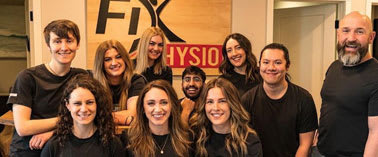 A group of people in black shirts are posing for a photo in front of a sign that says "Fix Physio".