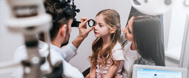 A child is getting an eye examination by a doctor using an ophthalmoscope.