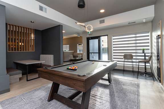 A pool table is in the middle of a room with a chair and a bar stool.at Vibe Apartments at Arbour Lake, Calgary, AB