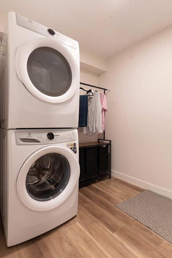 A white front loading washing machine is stacked on top of another one in a laundry room.at Vibe Apartments at Arbour Lake, Calgary