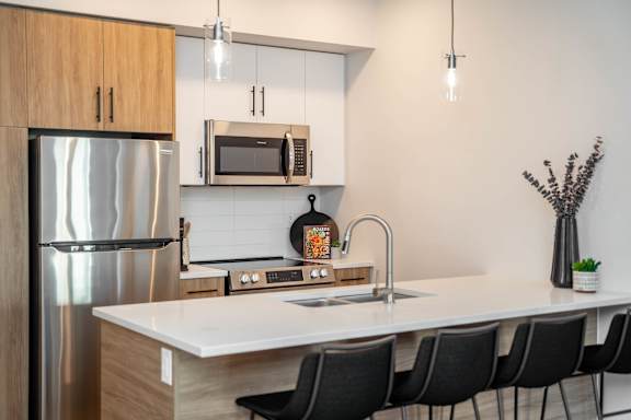 A modern kitchen with a white countertop and black chairs.at Vibe Apartments at Arbour Lake, Alberta, T3G 4J2